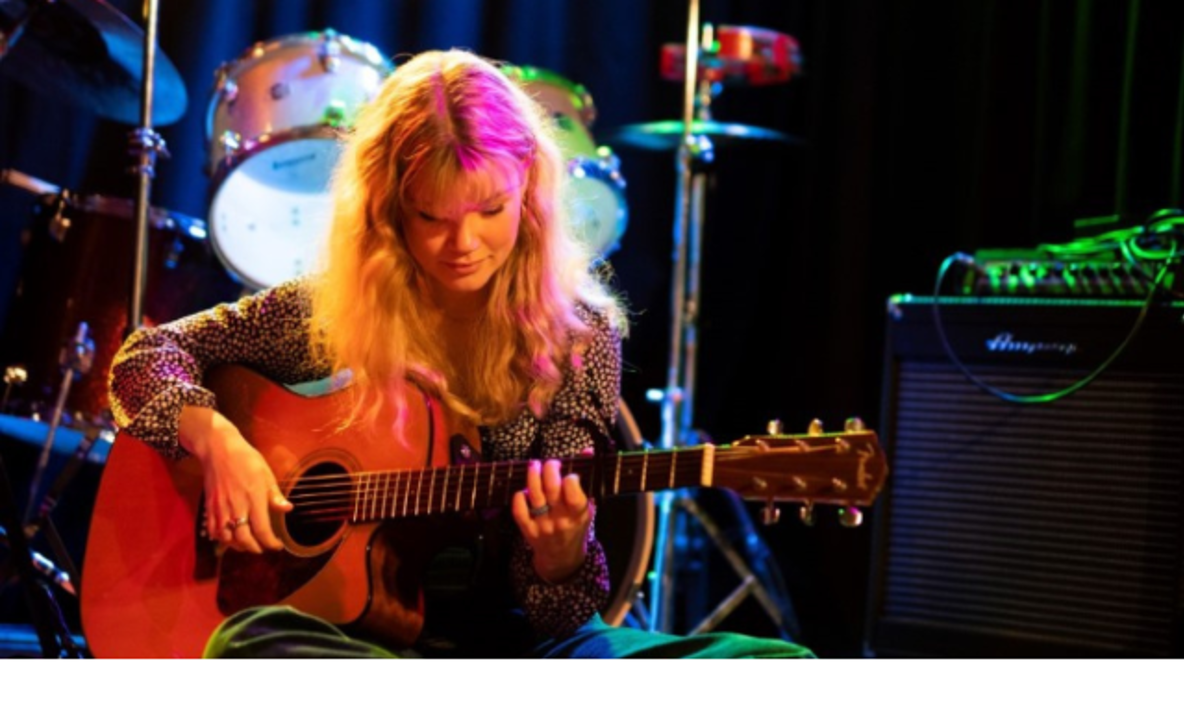En person sitter ner och spelar gitarr.