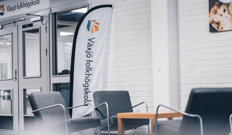 Beachflagga med texten Växjö folkhögskola, bakom grupp med fotöljer.
